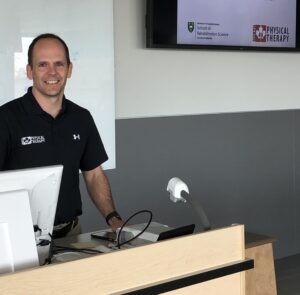 Kregg a Physiotherapy standing behind a desk while teaching course at the University of Saskatoon