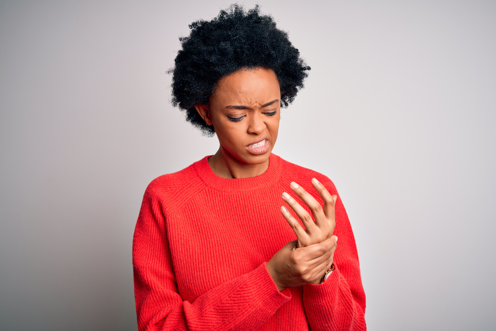 Lady grimacing in pain holding left hand and wrist due to inflammation possibly caused by de Quervain's Tenosynovitis