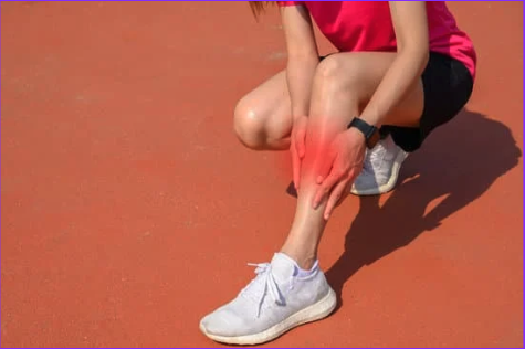 Woman holding lower leg due to shin splints, shin area is highlighted red.