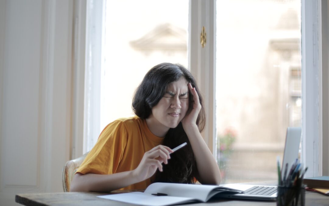 Lady trying to manage vestibular migraines and regain balance while sitting at a desk holding her head in pain.